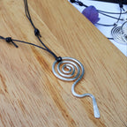 Silver spiral pendant on a black cord against a wooden background