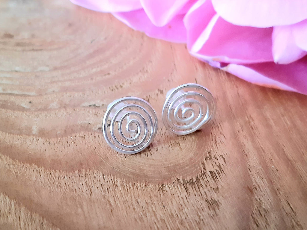 Silver spiral earrings on a wooden surface with pink fabric in the background