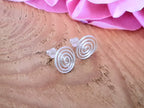 Silver spiral earrings on a wooden surface with pink flowers in the background