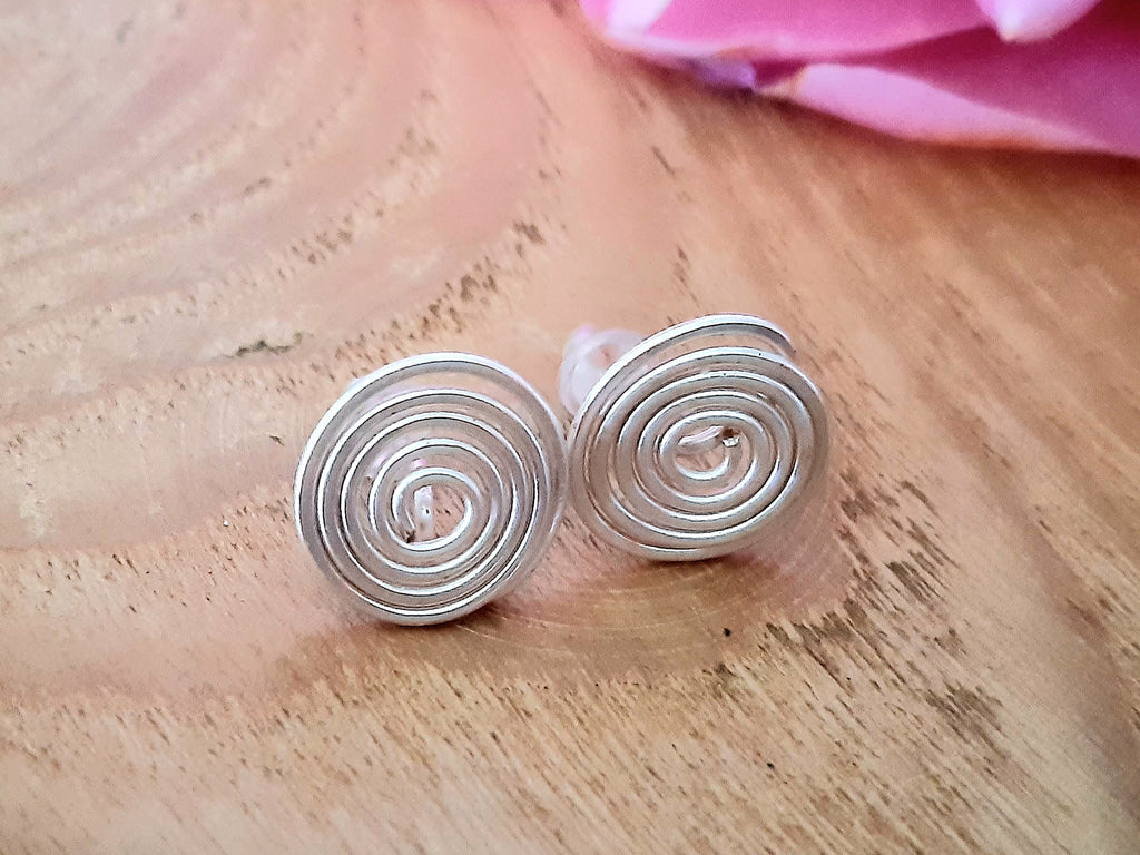 Silver spiral earrings on a wooden surface with a pink flower in the background