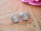 Silver spiral earrings on a wooden surface with a pink flower in the background