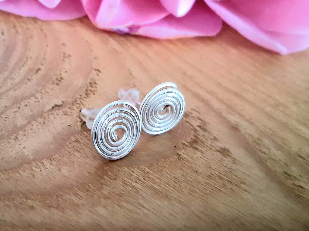 Silver spiral earrings on a wooden surface with pink fabric in the background