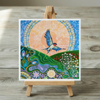 Colourful artwork of a swallow bird flying over a landscape with flowers on a wooden easel.
