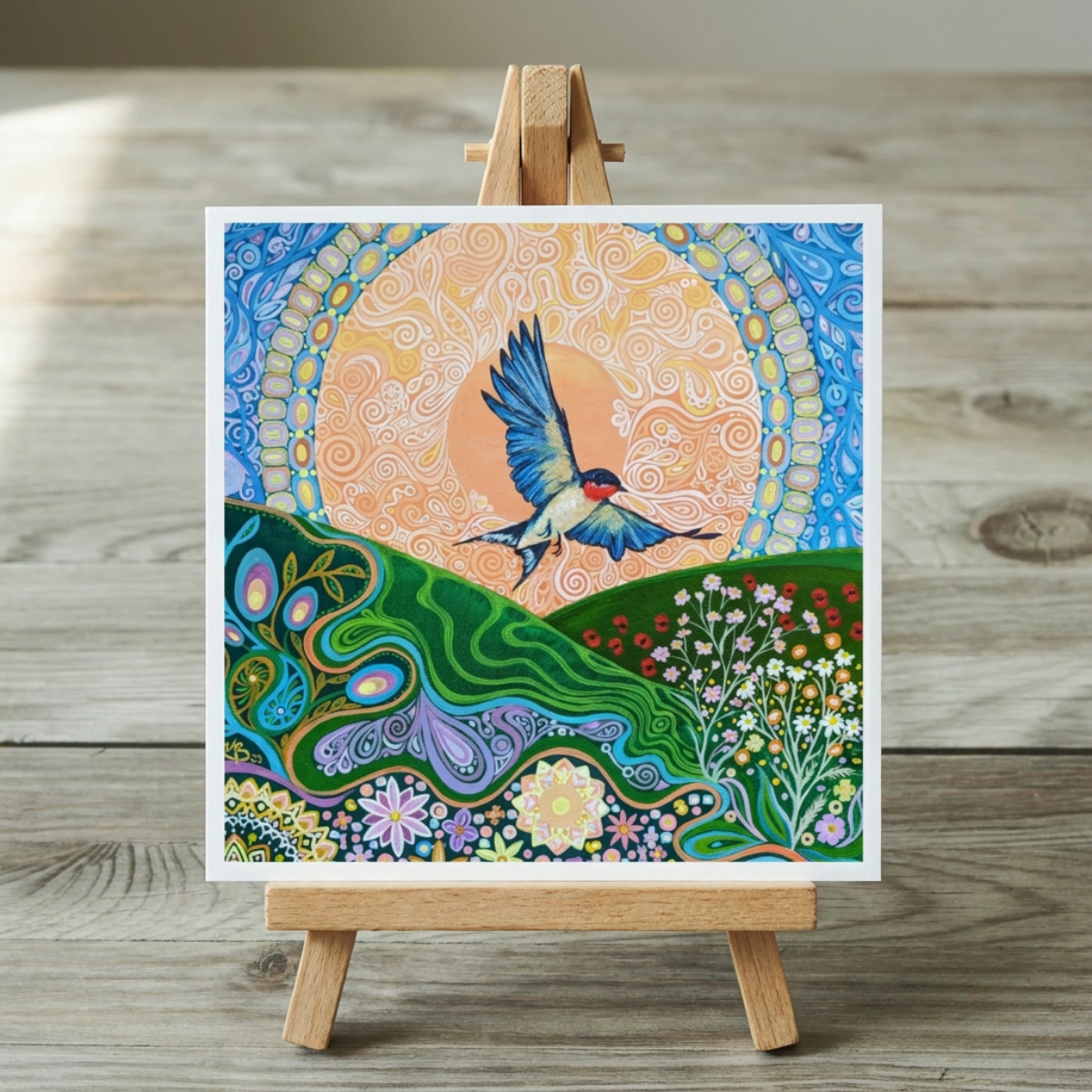 Colourful artwork of a swallow bird flying over a landscape with flowers on a wooden easel.