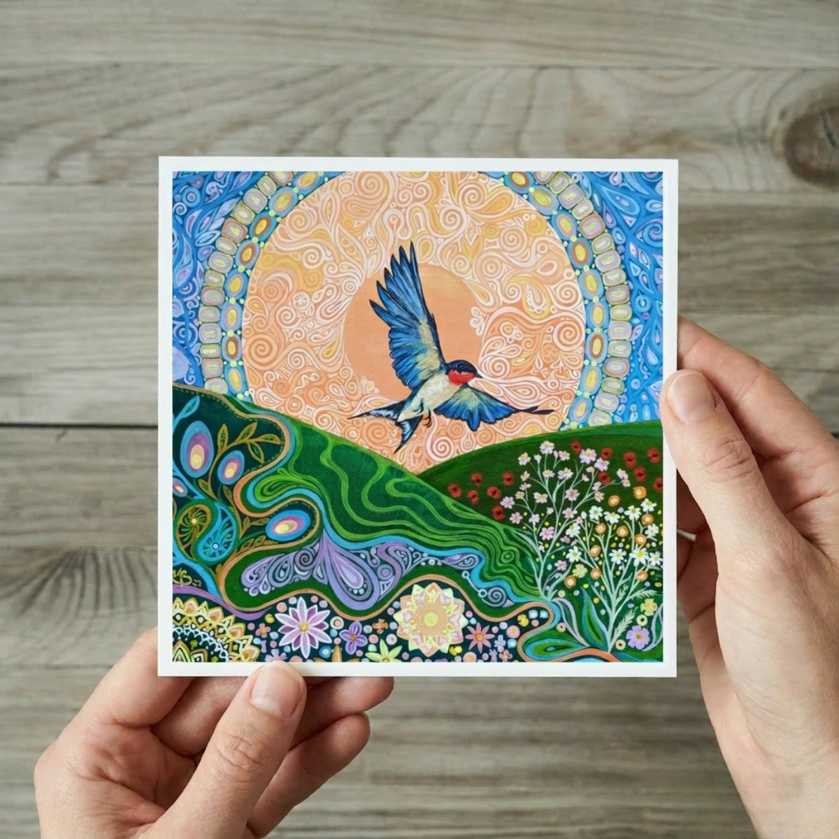Colourful abstract artwork of a swallow bird in flight held by hands on a wooden surface