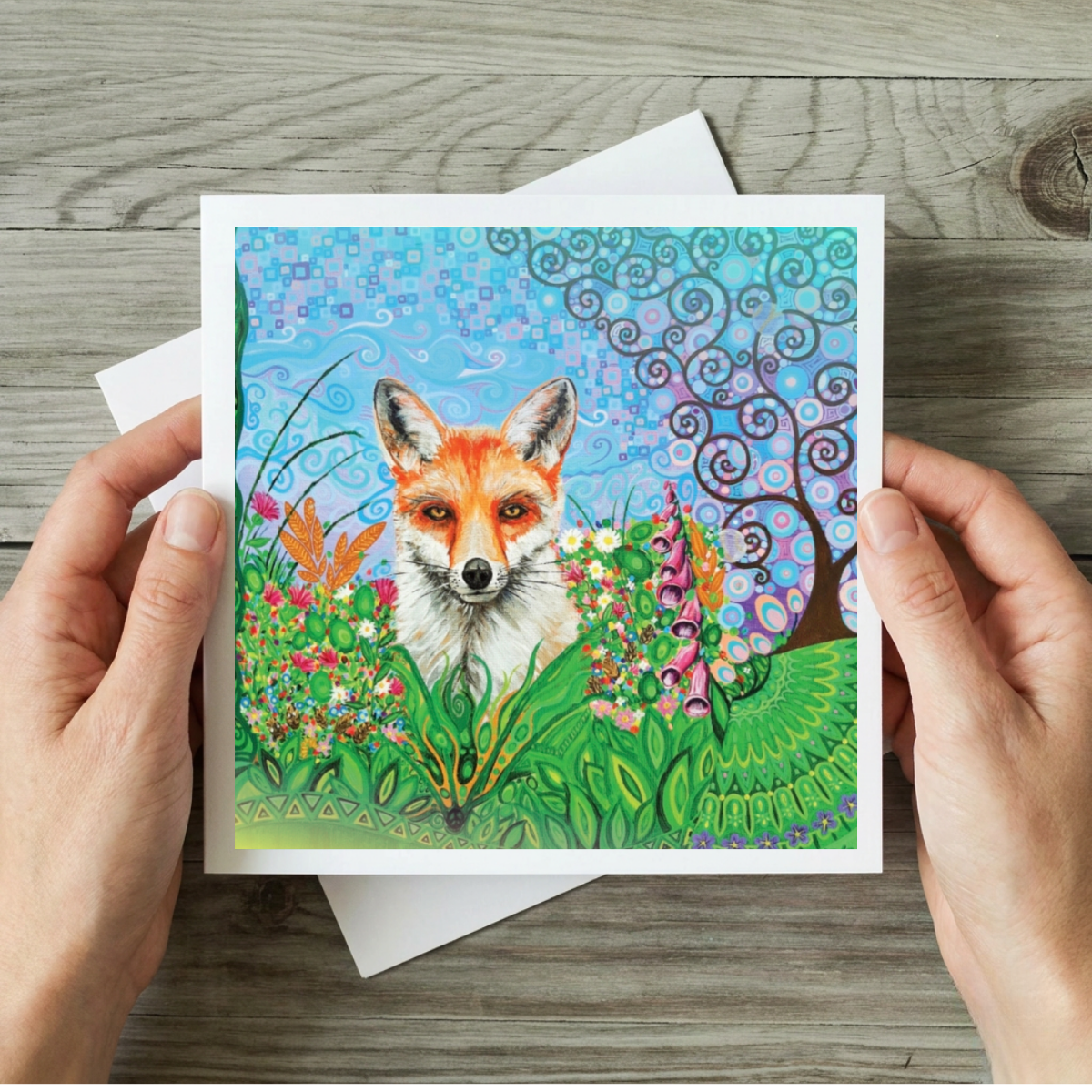 Greeting card with a fox illustration held by hands on a wooden surface