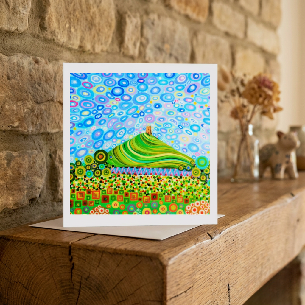 Colourful abstract artwork of Glastonbury Tor greeting card on a wooden surface with a stone wall background