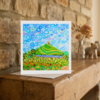 Colourful abstract artwork of Glastonbury Tor greeting card on a wooden surface with a stone wall background