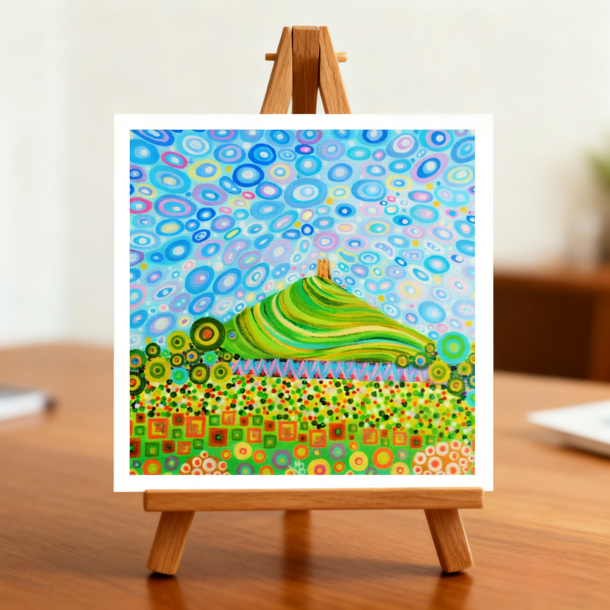 Colourful abstract painting of Glastonbury Tor on a greeting card on a small easel with a wooden base.