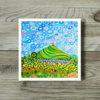 Colourful abstract painting of a green hill with a blue sky on a wooden surface