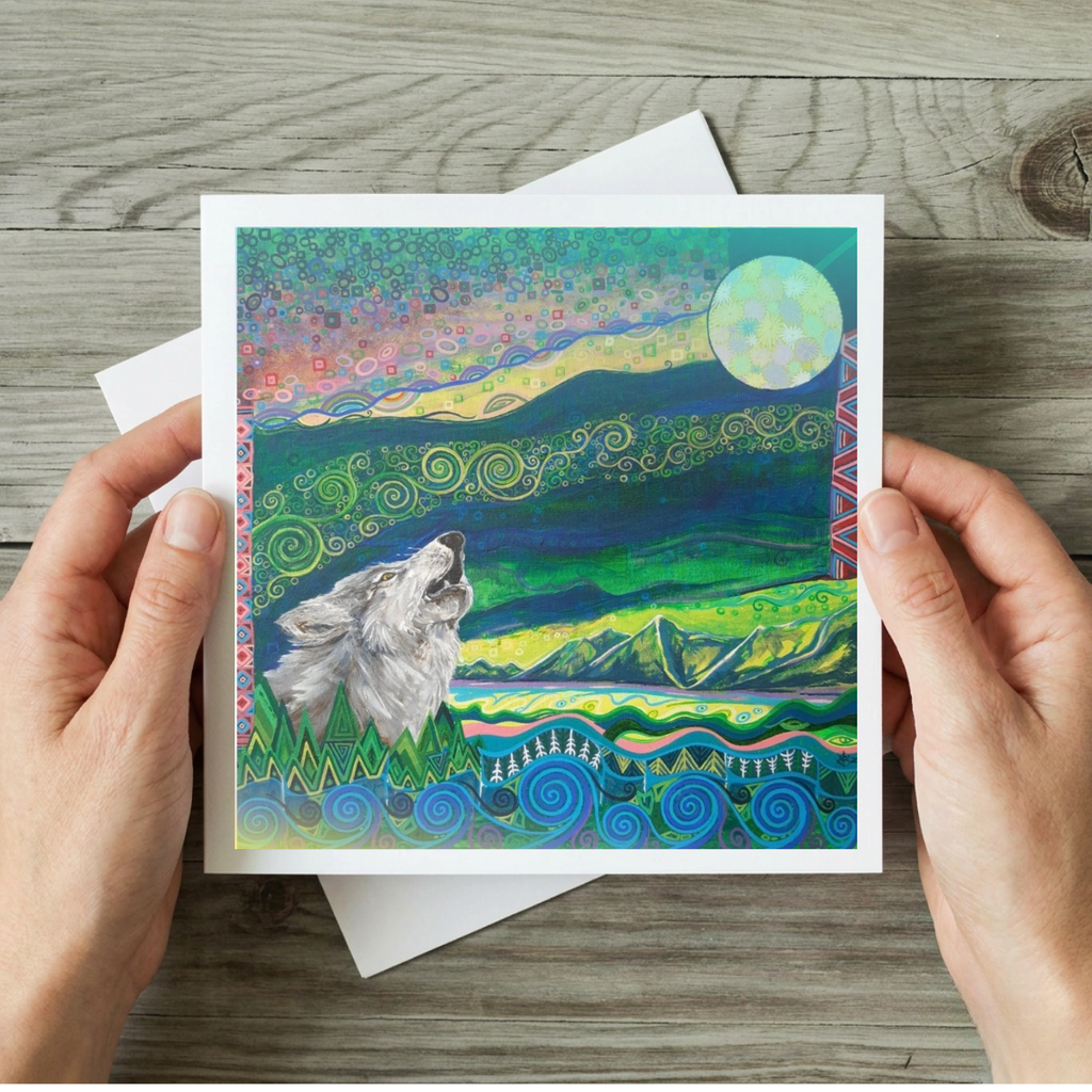 Greeting card with a wolf and mountain design held by hands on a wooden surface