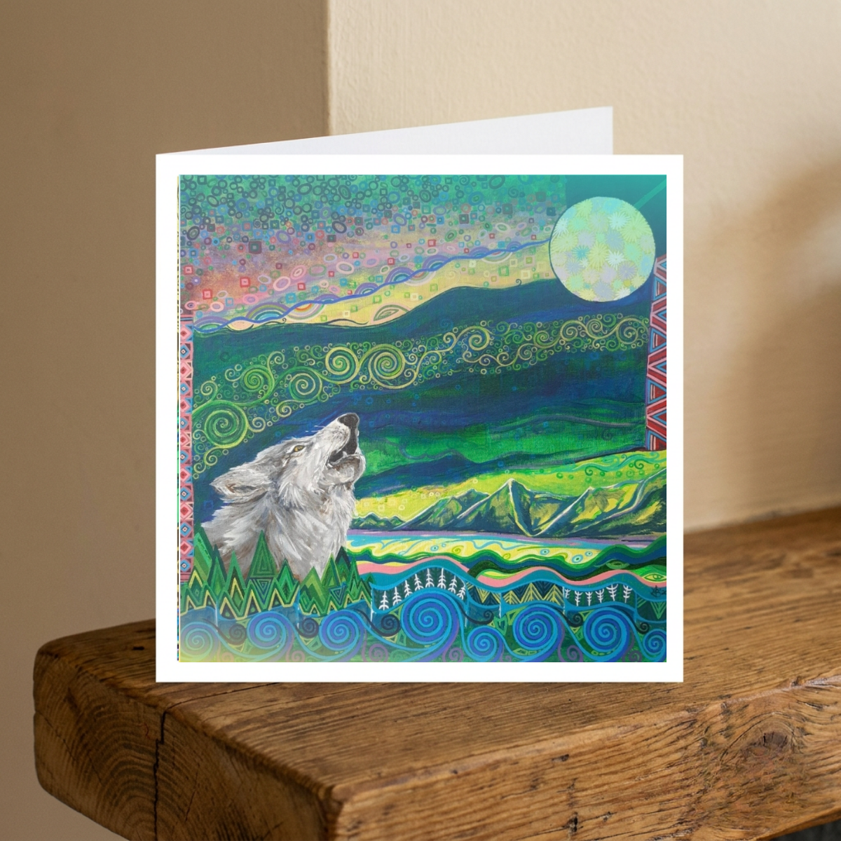 Greeting card with a wolf howling at the moon design on a wooden surface.