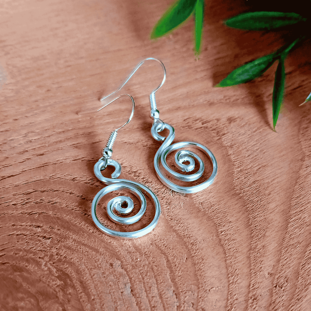 Silver spiral earrings on a wooden surface with green leaves.
