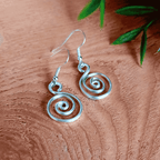 Silver spiral earrings on a wooden surface with green leaves.