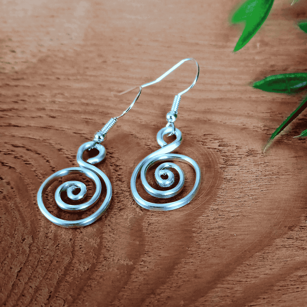 Silver spiral earrings on a wooden surface with green leaves.