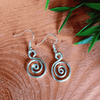 Silver spiral earrings on a wooden surface with green leaves.