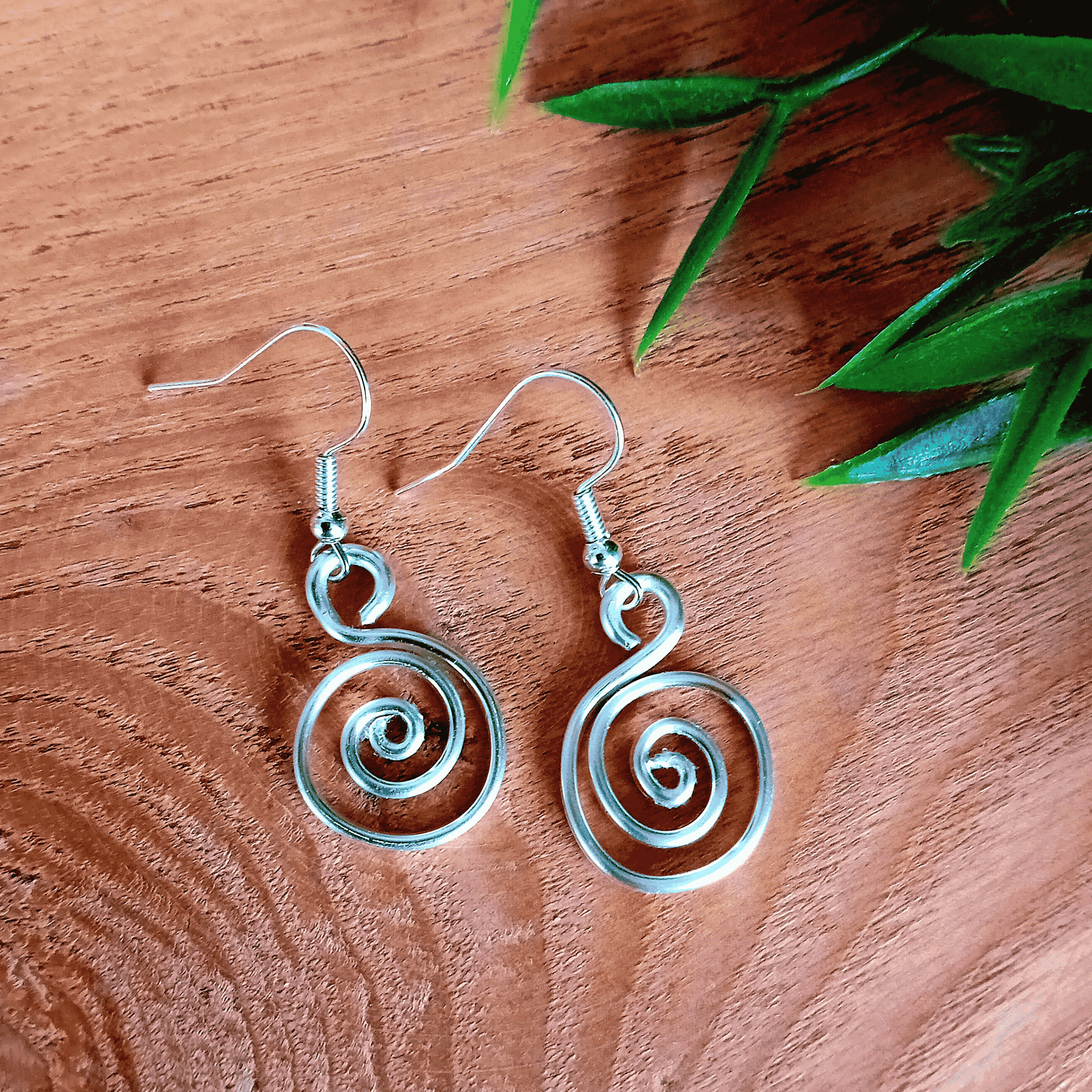 Silver spiral earrings on a wooden surface with green leaves.