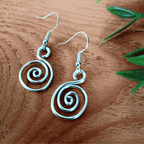 Silver spiral earrings on a wooden surface with green leaves.