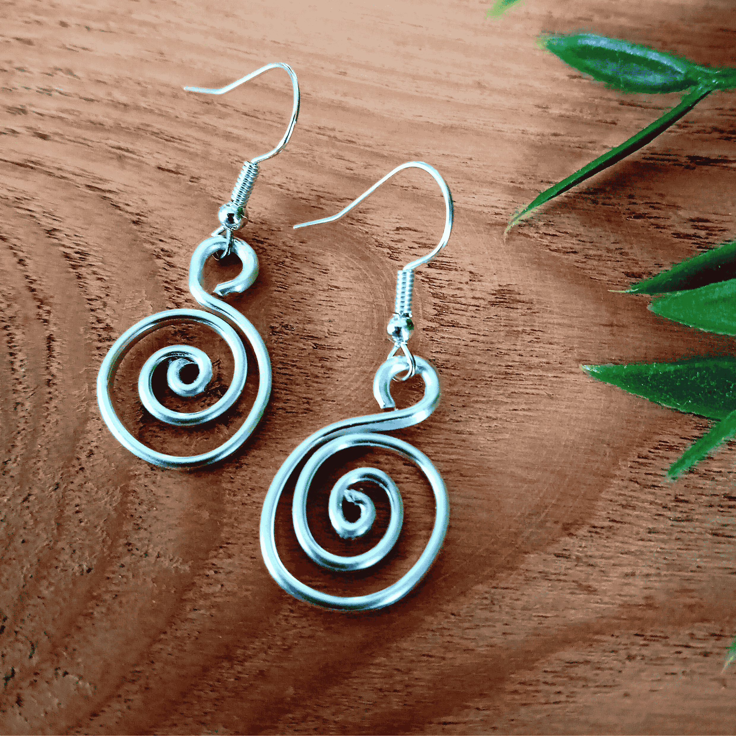 Silver spiral earrings on a wooden surface with green leaves.