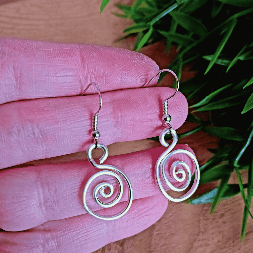 Silver spiral earrings on a pink hand with green leaves in the background