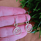 Silver spiral earrings on a pink hand with green leaves in the background