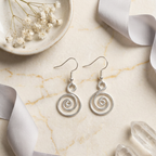 Silver spiral earrings on a marble surface with decorative elements.