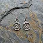 Silver spiral earrings on a textured stone surface