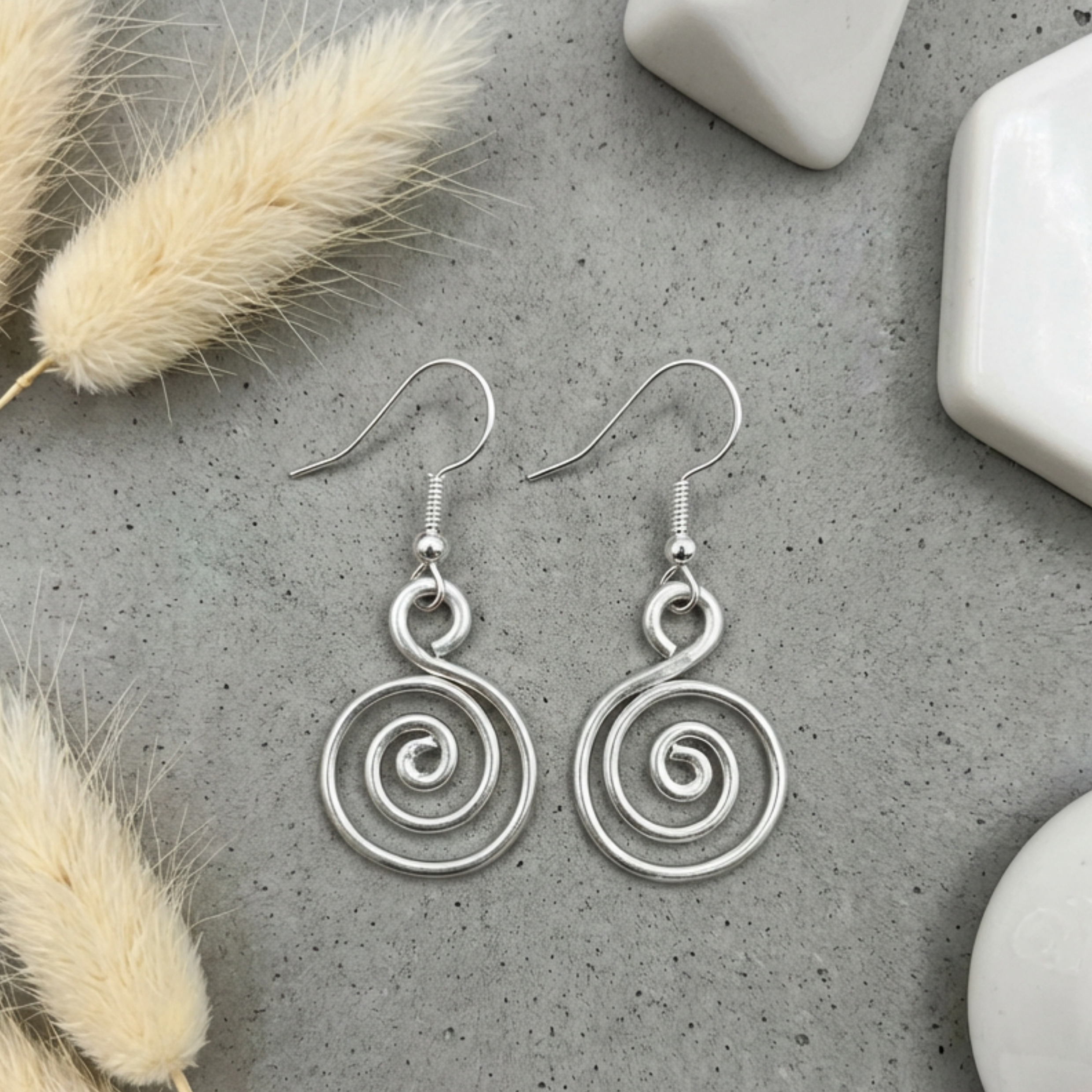 Silver spiral earrings on a grey surface with decorative elements.