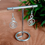 Silver spiral earrings on a metal stand with a wooden background
