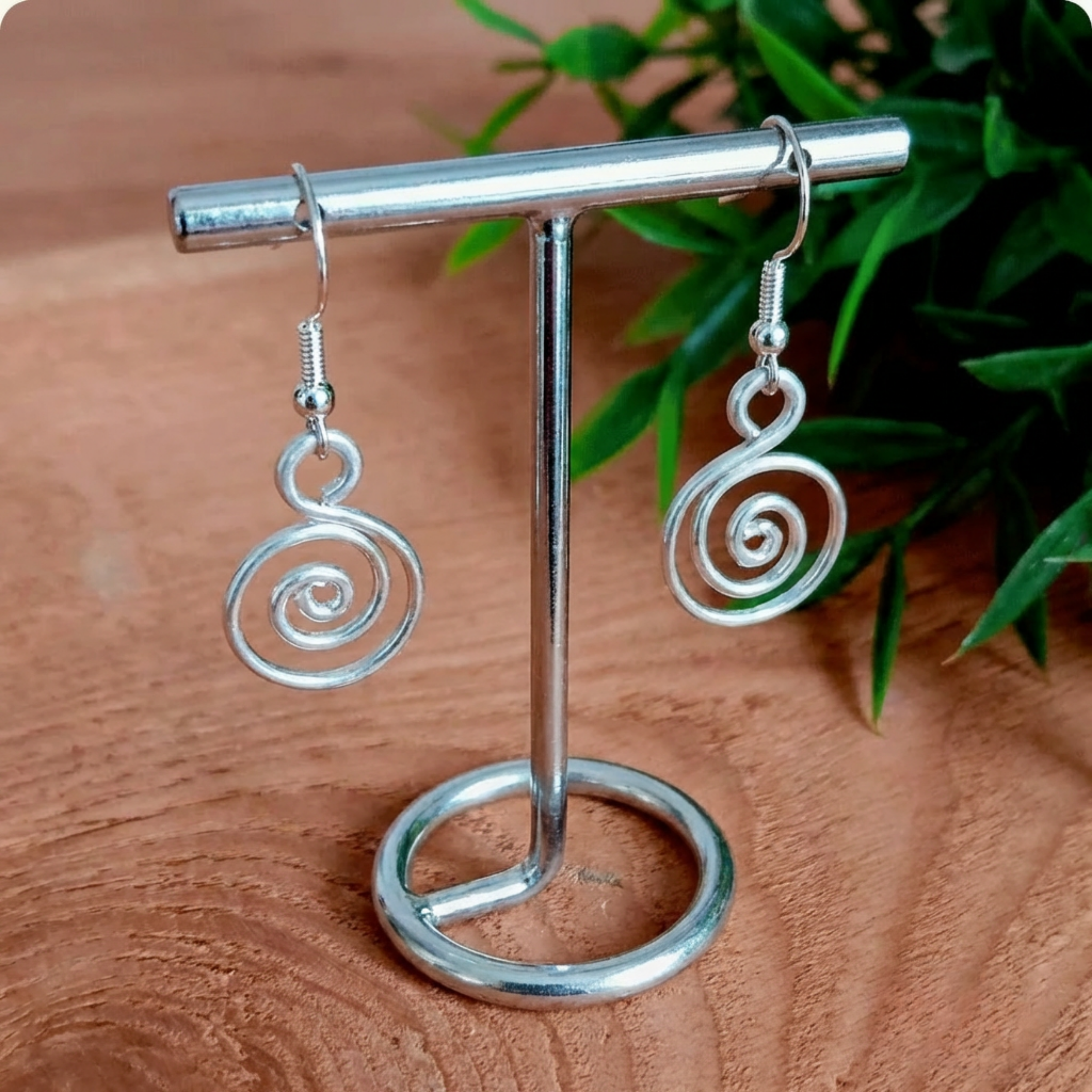 Silver spiral earrings on a metal stand with a wooden background