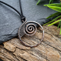 Copper spiral pendant on a black cord against a natural stone and wood background