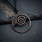 Copper Ammonite spiral pendant on a dark stone surface inspired by marine biology 