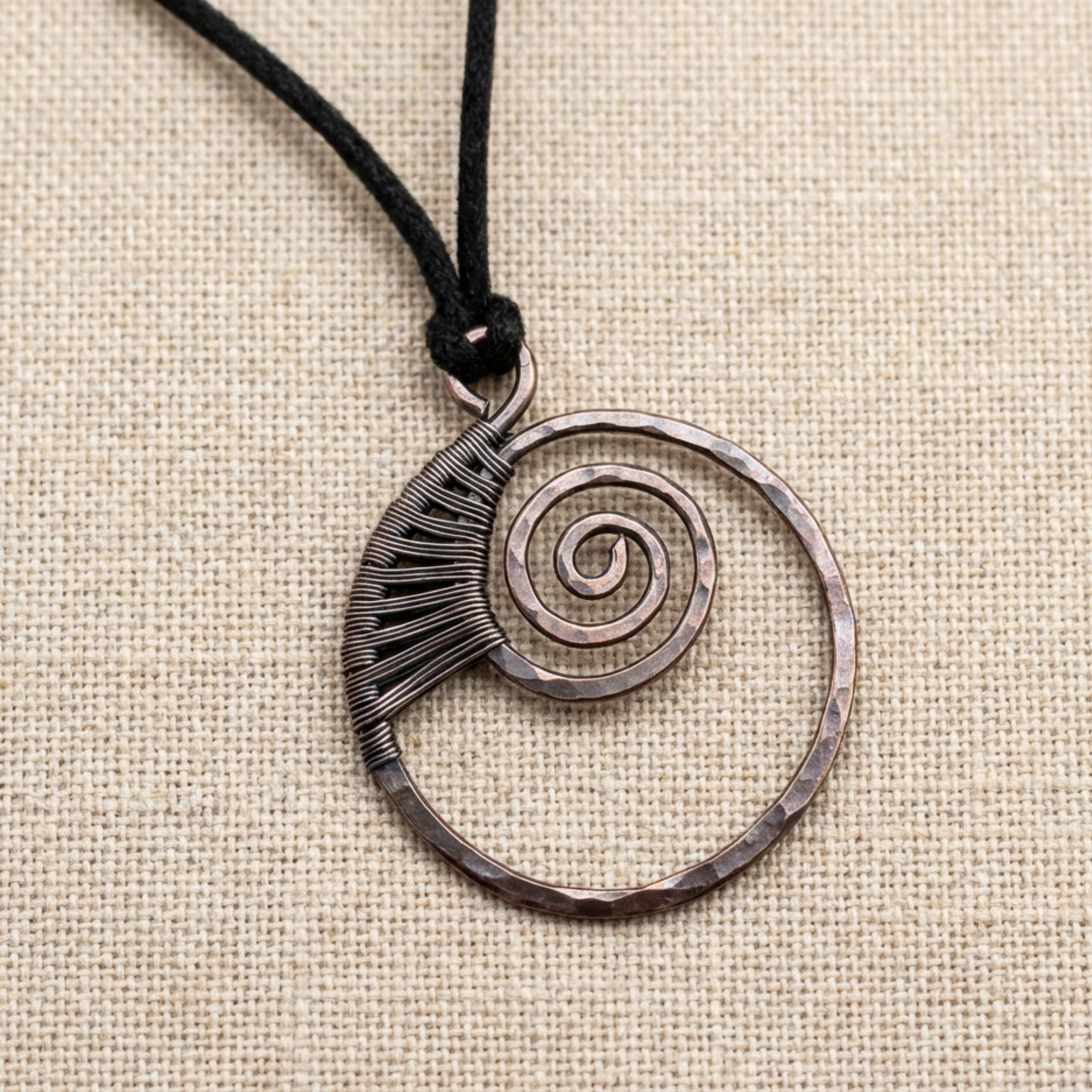 Copper spiral pendant on a black cord against a beige fabric background