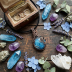 Jewelry set with a pendant, rings, and crystals on a wooden surface with flowers.