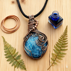 Blue stone pendant with copper wire wrapping on a wooden surface with leaves and ink bottle.