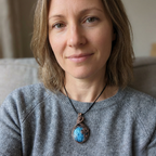 Woman wearing a gray sweater with a necklace featuring a blue pendant.