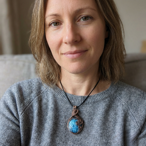 Woman wearing a gray sweater with a necklace featuring a blue pendant.