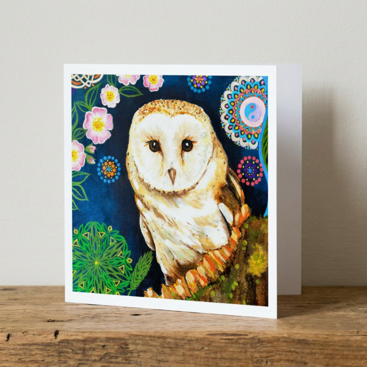 Greeting card with a painted owl and floral designs on a wooden surface.