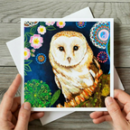 Greeting card with an owl design held by hands on a wooden surface