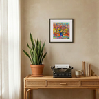 Decorative setup with a potted plant, typewriter, and books on a wooden table against a beige wall with a colorful abstract painting.