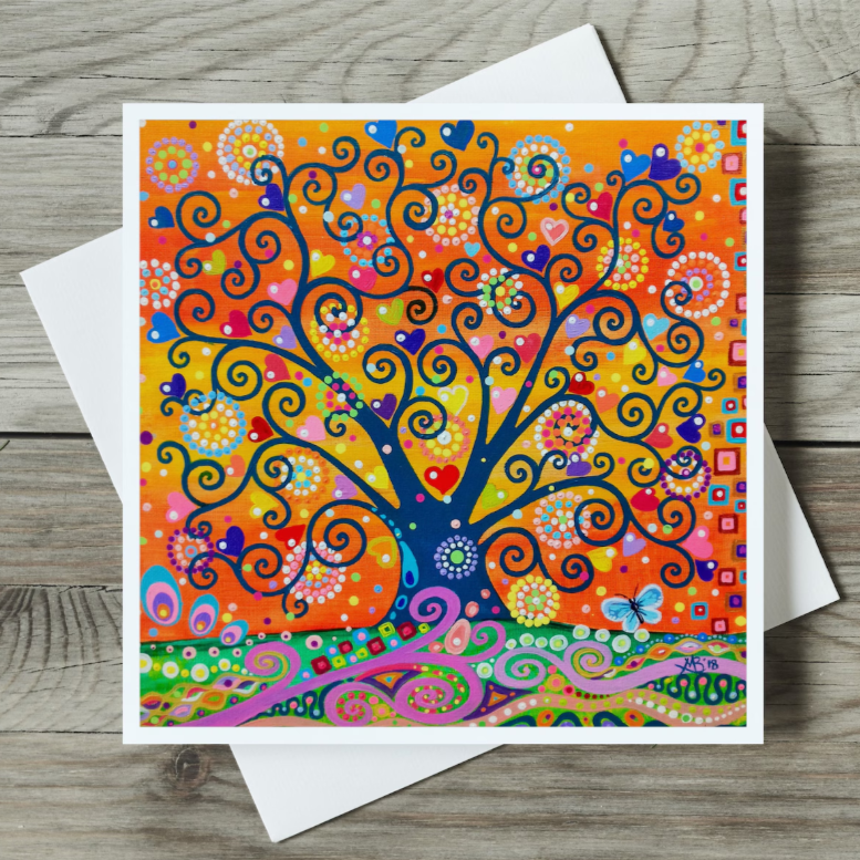 Colourful tree of life design on a card with a white envelope on a wooden surface