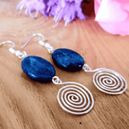 Pair of earrings with blue stones and silver spiral designs on a wooden surface.