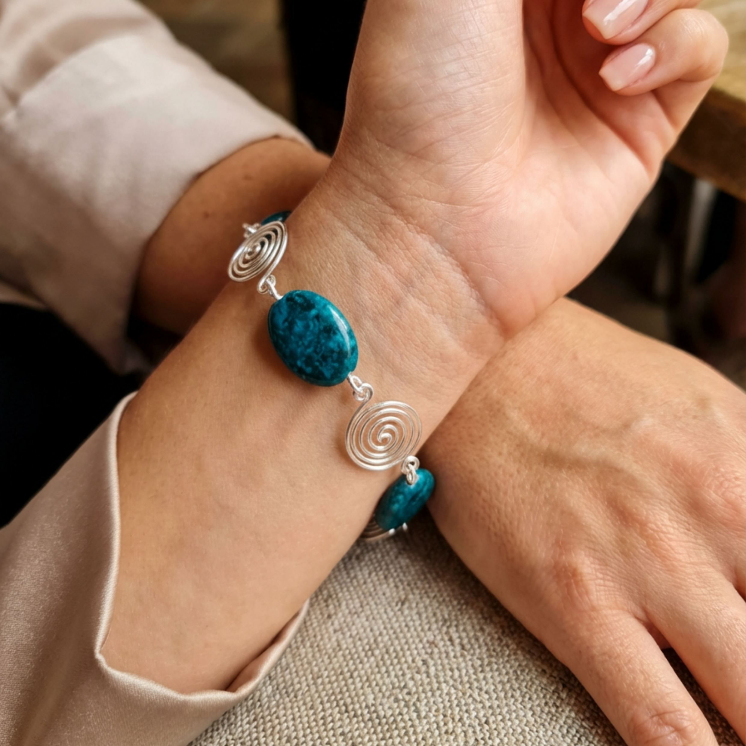 Close-up of a hand wearing a bracelet with blue beads and silver spiral designs.