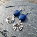Silver spiral earrings with blue stones on a stone surface