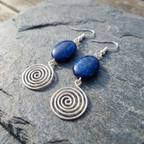 Silver spiral earrings with blue stones on a stone surface