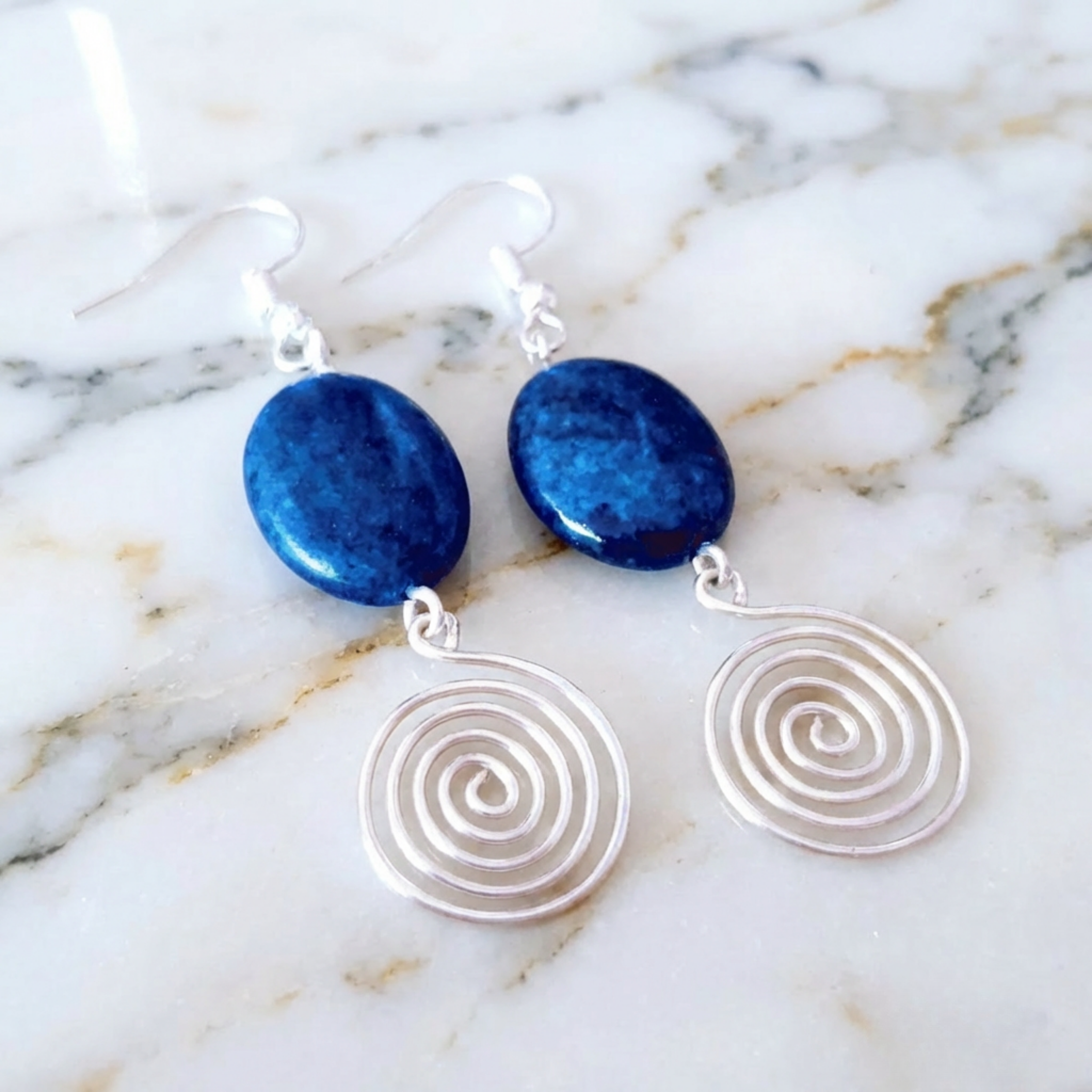 Earrings with blue stones and silver spiral designs on a marble background