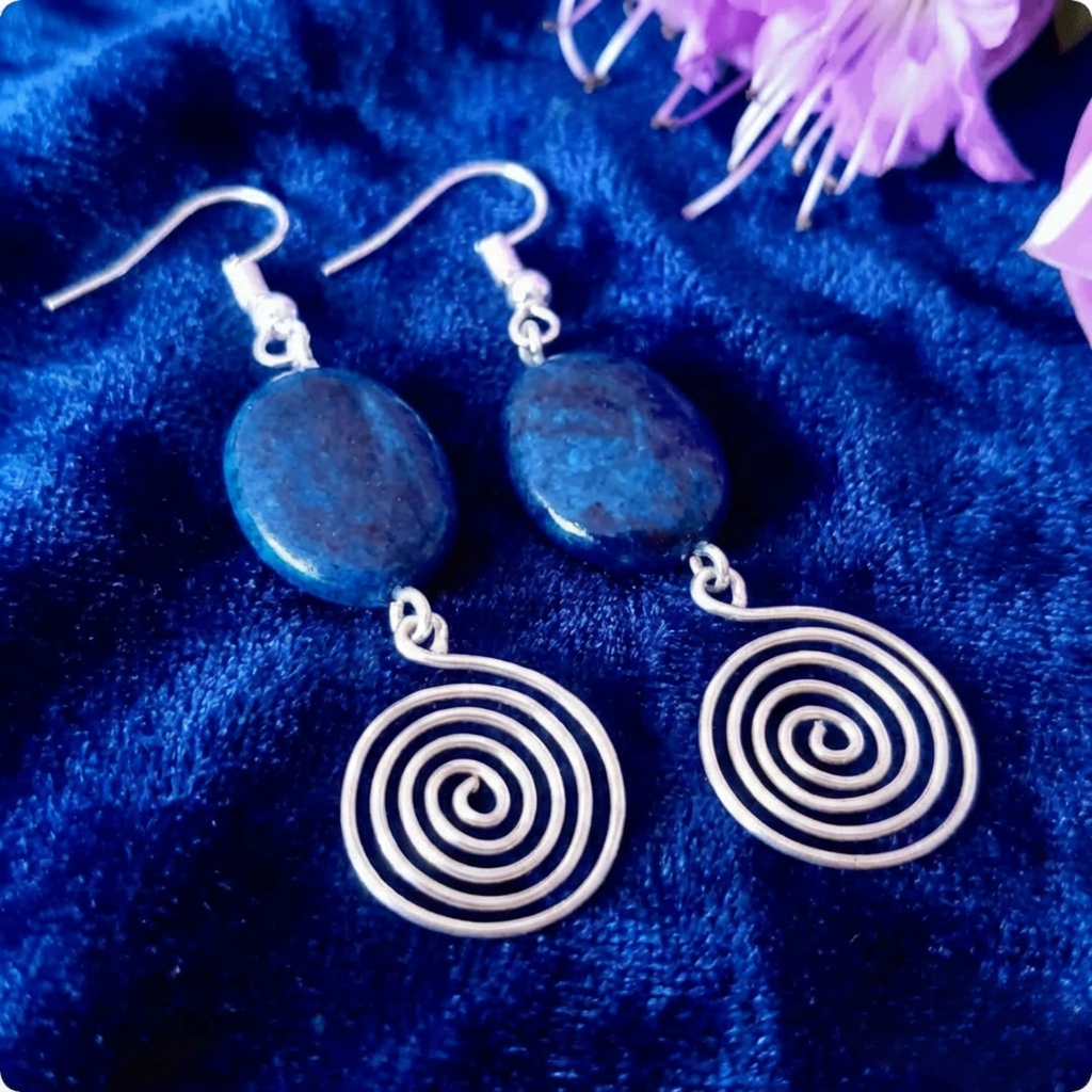Silver spiral earrings on a blue fabric background with purple flowers.