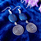 Silver spiral earrings on a blue fabric background with purple flowers.