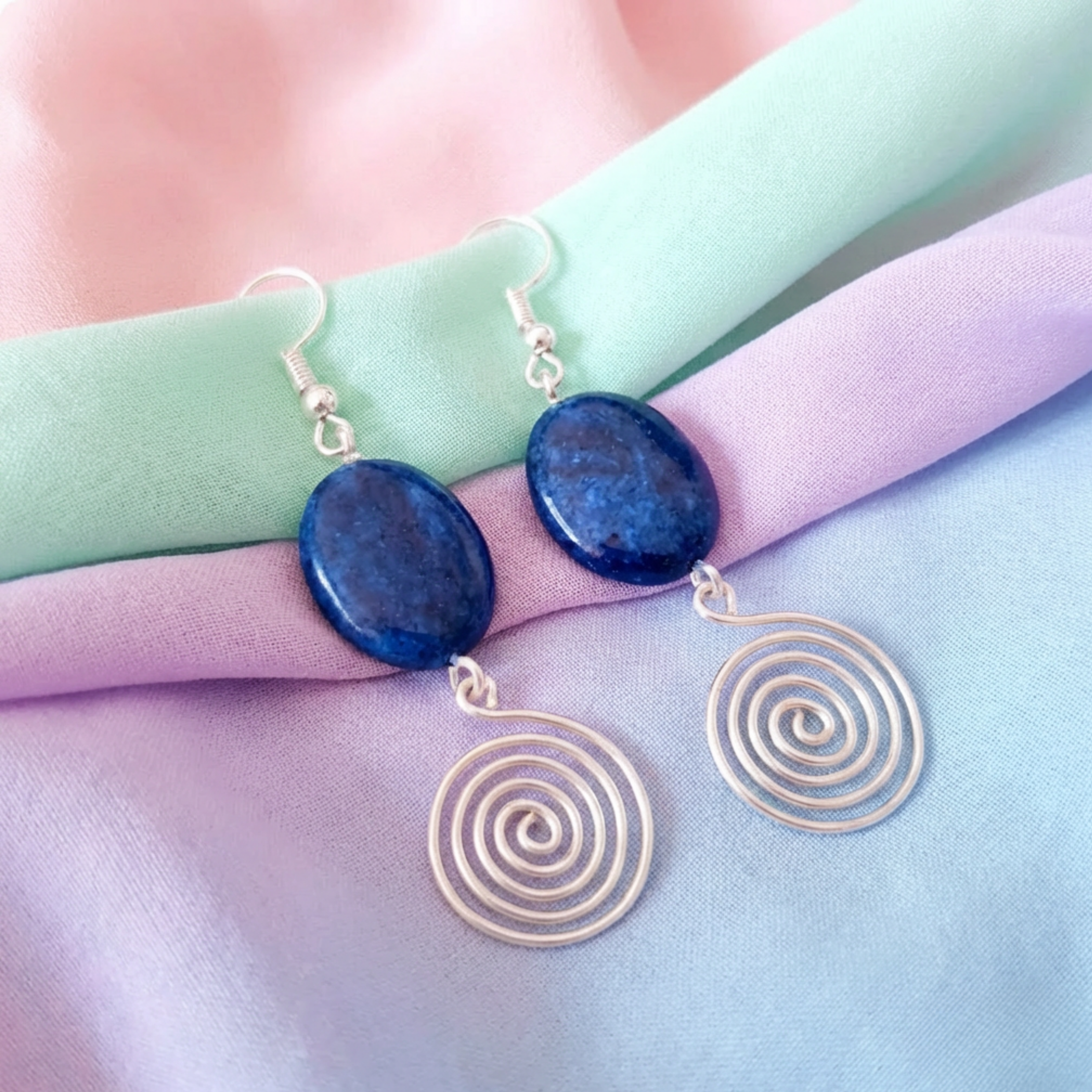 Pair of earrings with blue stones and gold spiral designs on a pastel fabric background