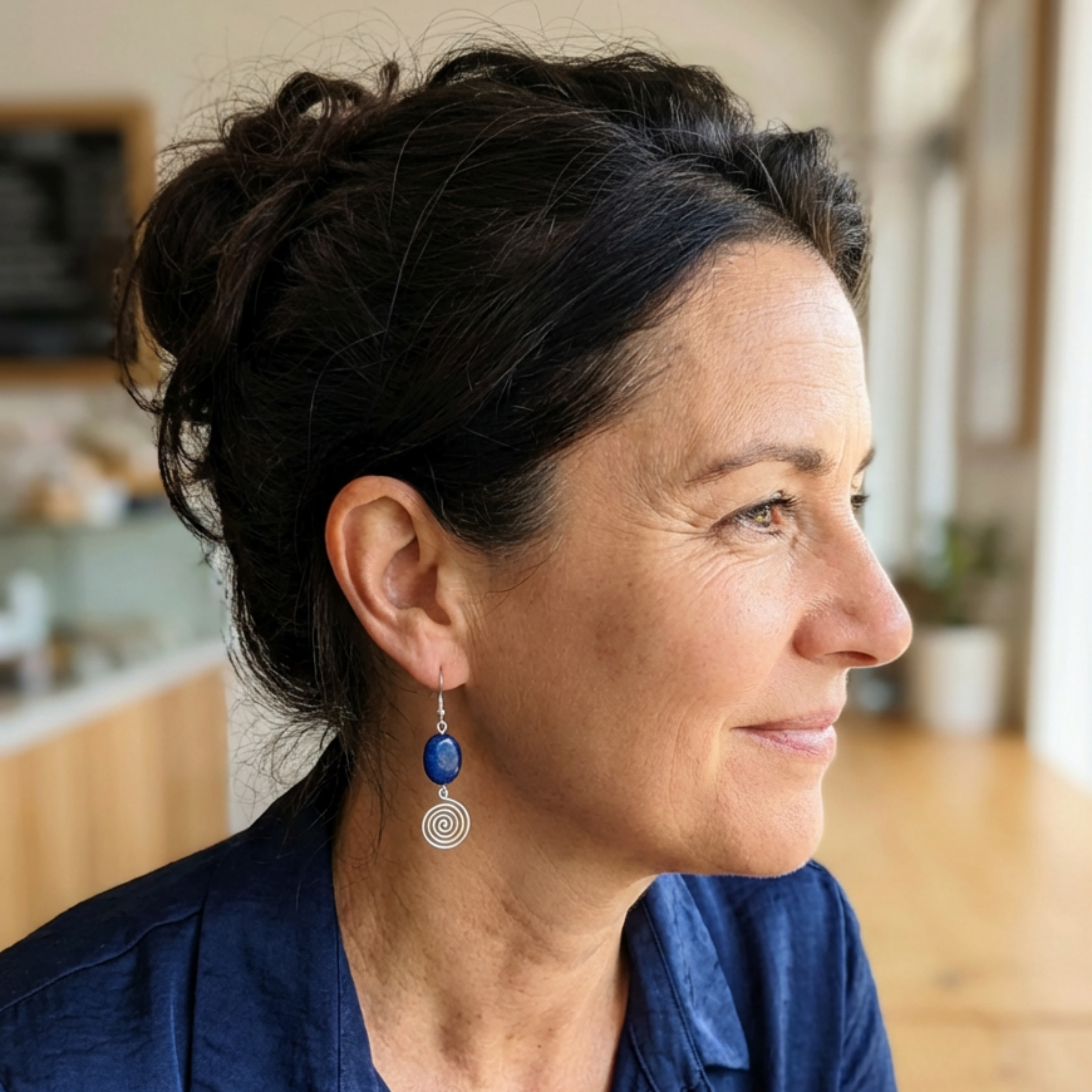 Woman wearing blue earrings with silver spirals in a blurred indoor setting